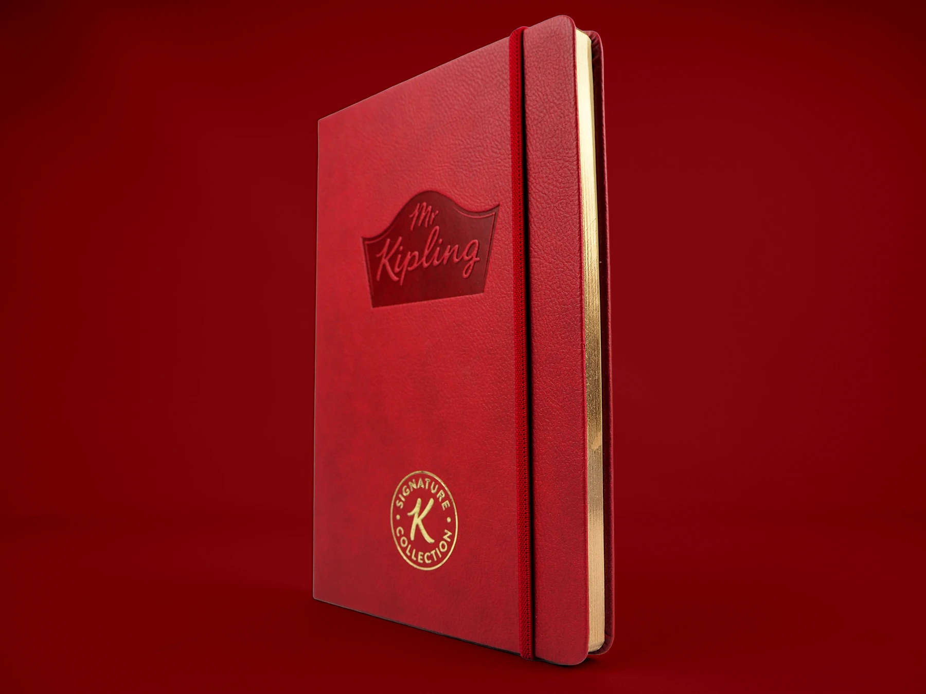 Custom Mr Kipling bespoke notebook in red. The Mr Kipling logo is debossed and there is a foil printed stamp at the bottom.