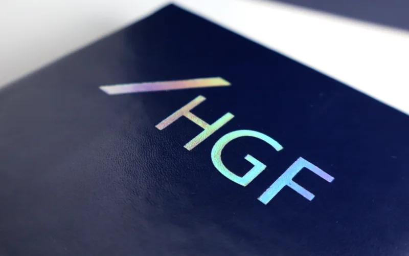 Close-up of a dark blue surface featuring the iridescent letters HGF with a diagonal line above the letters.