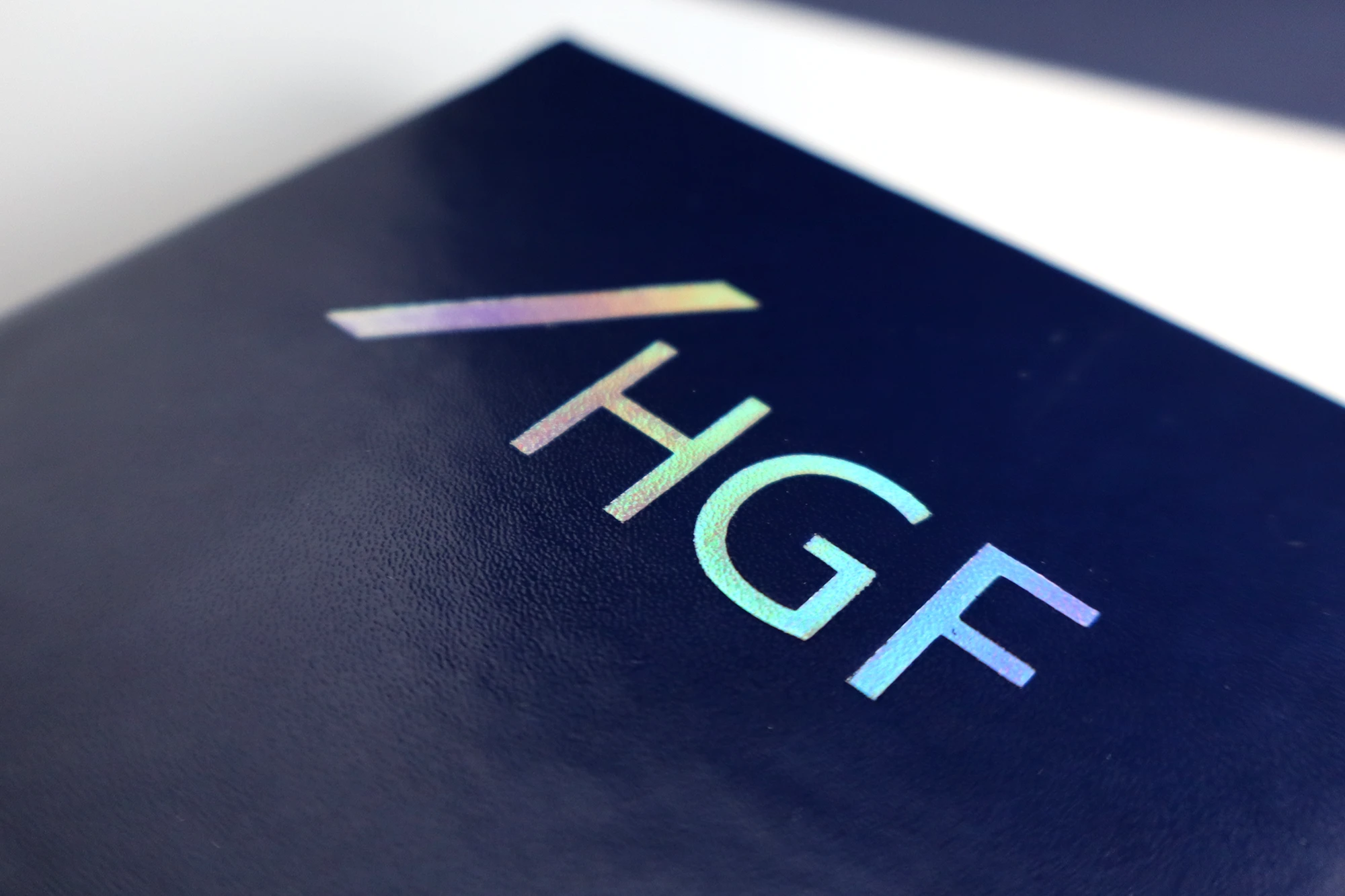 Close-up of a dark blue surface featuring the iridescent letters HGF with a diagonal line above the letters.