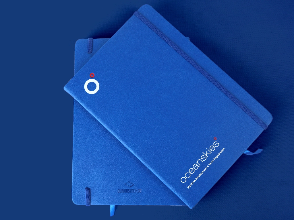 Branded ocean skies notebooks in bright blue, with white and red foil printed logo.