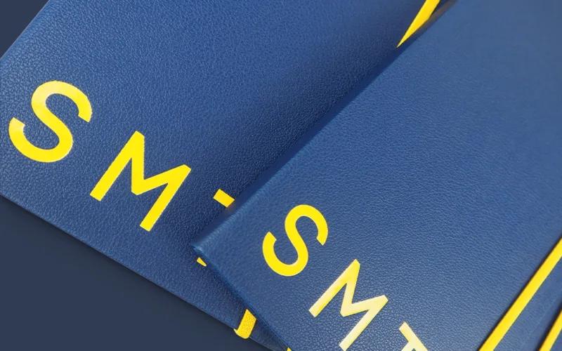 Close-up of blue textured folders or binders with bold yellow letters SMT partially visible on each cover, arranged in an overlapping pattern.