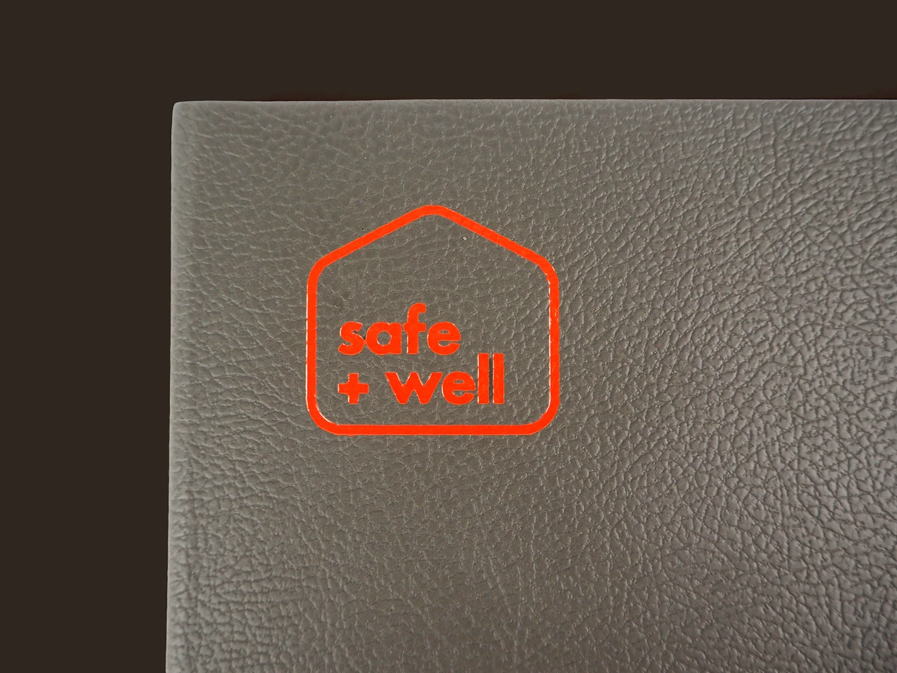 Close up of 'safe and well' motif on Cadent branded notebook. The notebook is dark grey and the motif is foil printed in a bright orange.