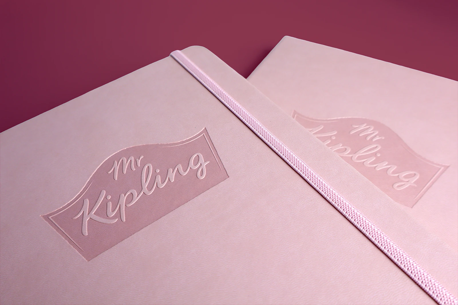 Mr Kipling branded notebook in Baby Pink. The logo is debossed in the top center of the notebook.