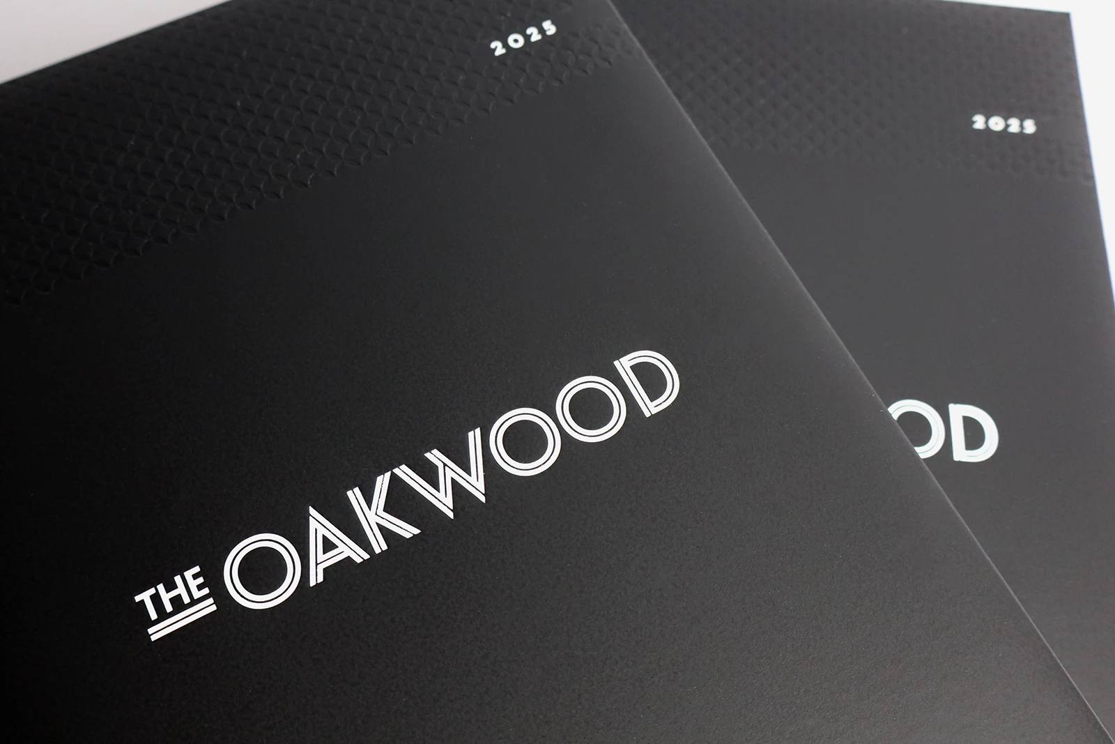 Oakwood custom diaries. They are black and have the logo printed on in white. There is a debossed geometric pattern strip at the top.
