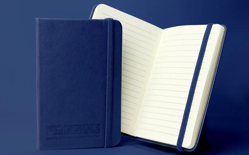 A blue leather notebook featuring the OSCE logo and the text 